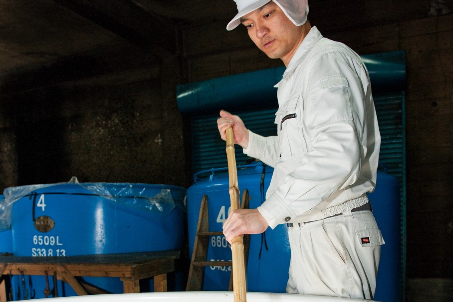 大分県豊後大野市の牟礼鶴酒造で焼酎の仕込み作業を行う職人。SHUSHUの陶器ボトルに詰められる長期貯蔵麦焼酎を丁寧に仕込む様子。