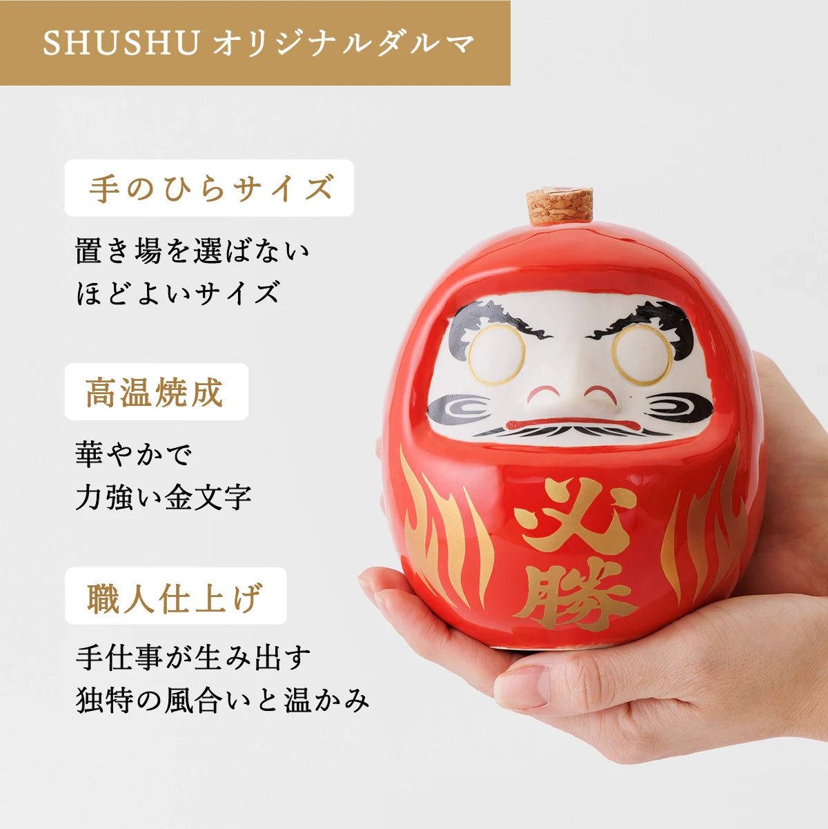 名入れ酒器ギフトSHUSHU。手のひらサイズの赤いダルマ型陶器ボトルに『必勝』の金文字。高温焼成と職人仕上げ。華やかな縁起物