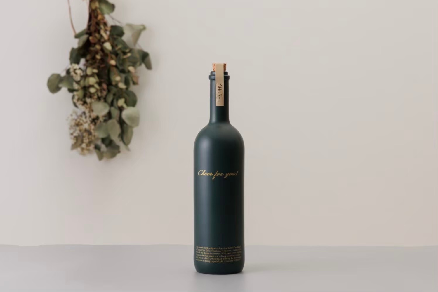 深緑のマット質感が上品な、美濃焼のストレート型陶器ボトル。金文字で「Cheer for you!」と描かれたデザインが印象的な、SHUSHUの名入れギフトボトル。