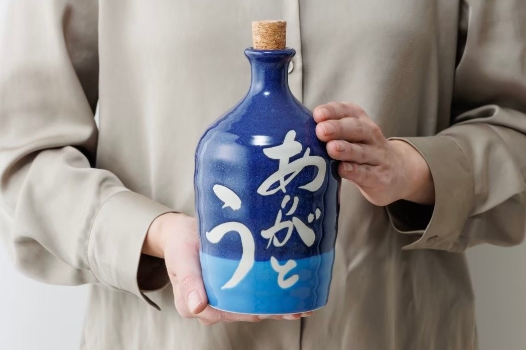 「ありがとう」と手描きされた藍色の名入れ陶器ボトルを両手で持つ様子。SHUSHUの職人が丁寧に仕上げた美濃焼ギフト。